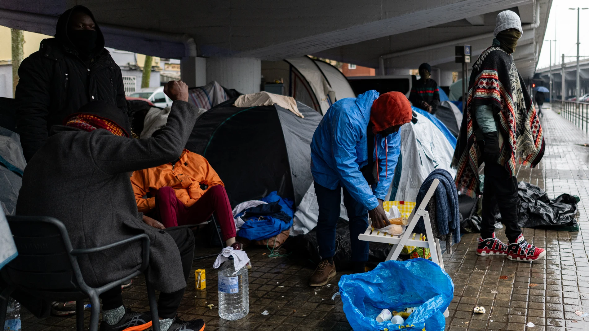 Personas desalojadas del antiguo Instituto B9 de Badalona acampan debajo de la salida 210 de la C-31, en el barrio de Sant Roc, a 20 de diciembre de 2025, en Badalona, Barcelona, Catalunya (España). Las fuertes lluvias que se han abierto paso en las últimas horas han provocado que cerca de una treintena de migrantes del grupo de desalojados el pasado miércoles del antiguo instituto B9 hayan tenido que refugiarse debajo del puente que sostiene el eje costero en el tramo que pasa por la ciudad...