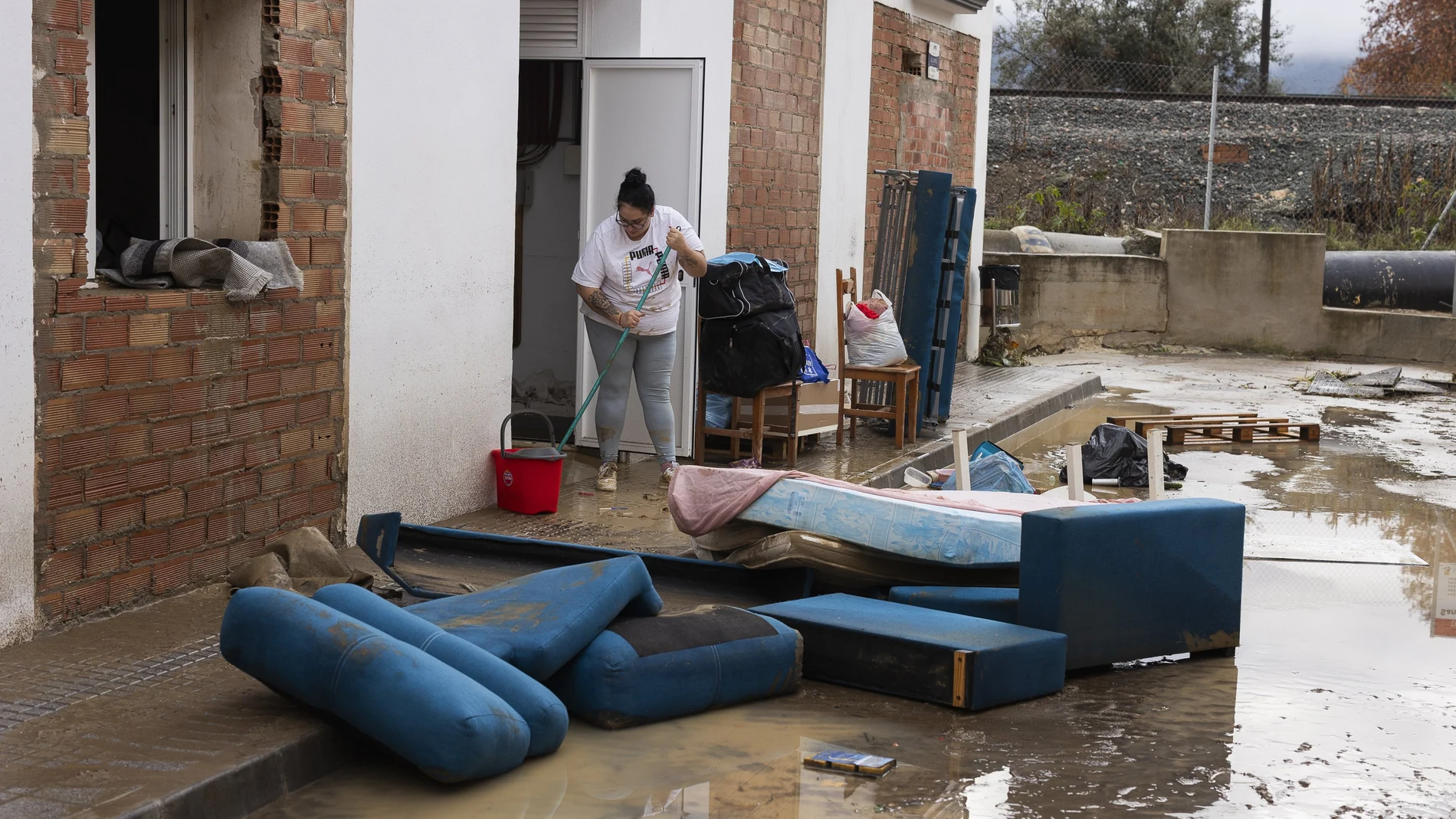 Una residente limpia la entrada de una vivienda, este domingo, en Estación de Cártama después de los problemas sufridos anoche en la localidad por la crecida del río. El temporal de lluvia que afecta a Andalucía, principalmente a Málaga, ha dejado por el momento 304 incidencias en esta provincia, donde se han producido algunos desalojos y rescates en los municipios de Alhaurín de la Torre y Cártama por inundaciones.