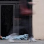 Varias personas pasan delante de una persona sin hogar en Barcelona