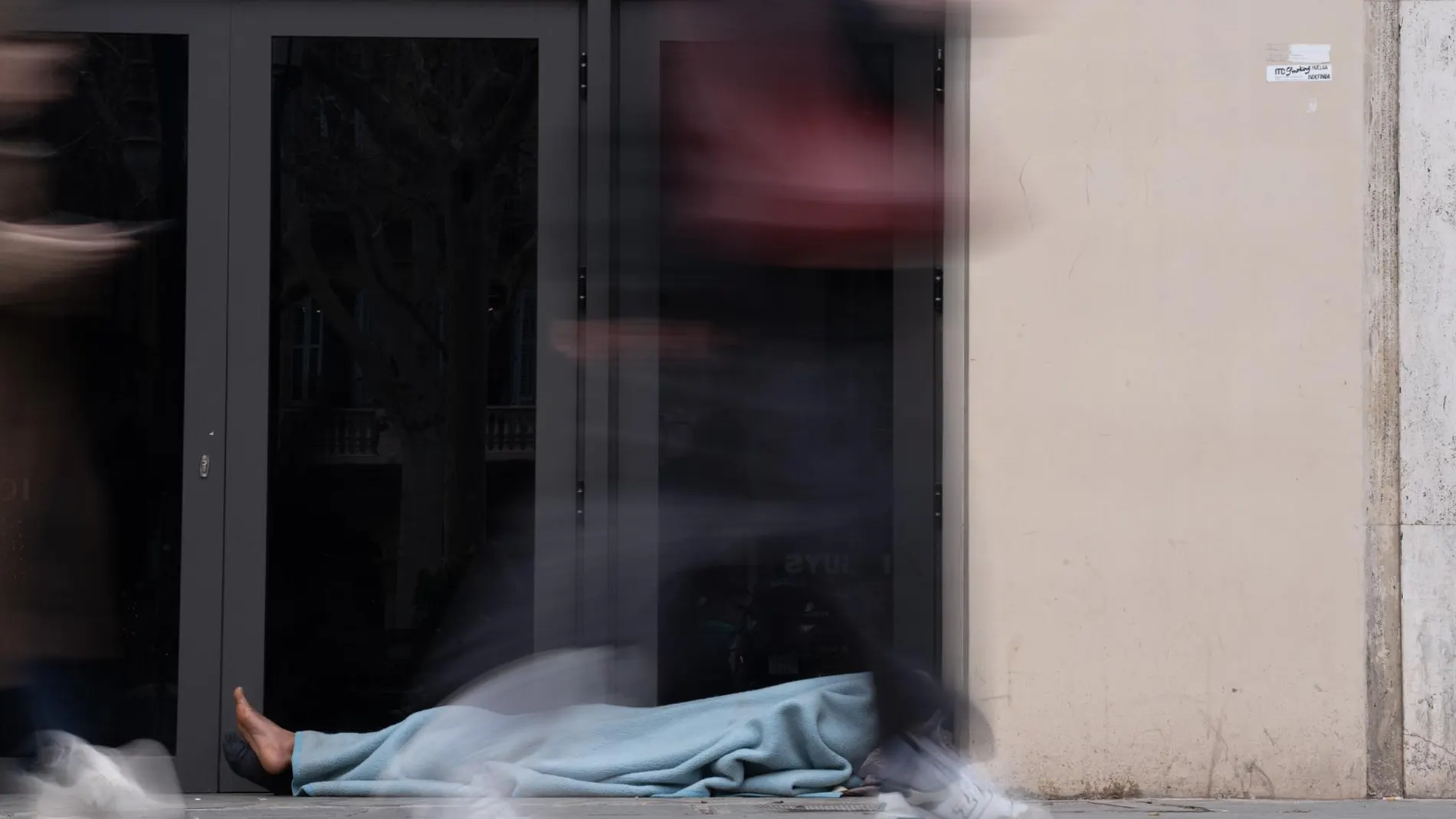 Varias personas pasan delante de una persona sin hogar en Barcelona