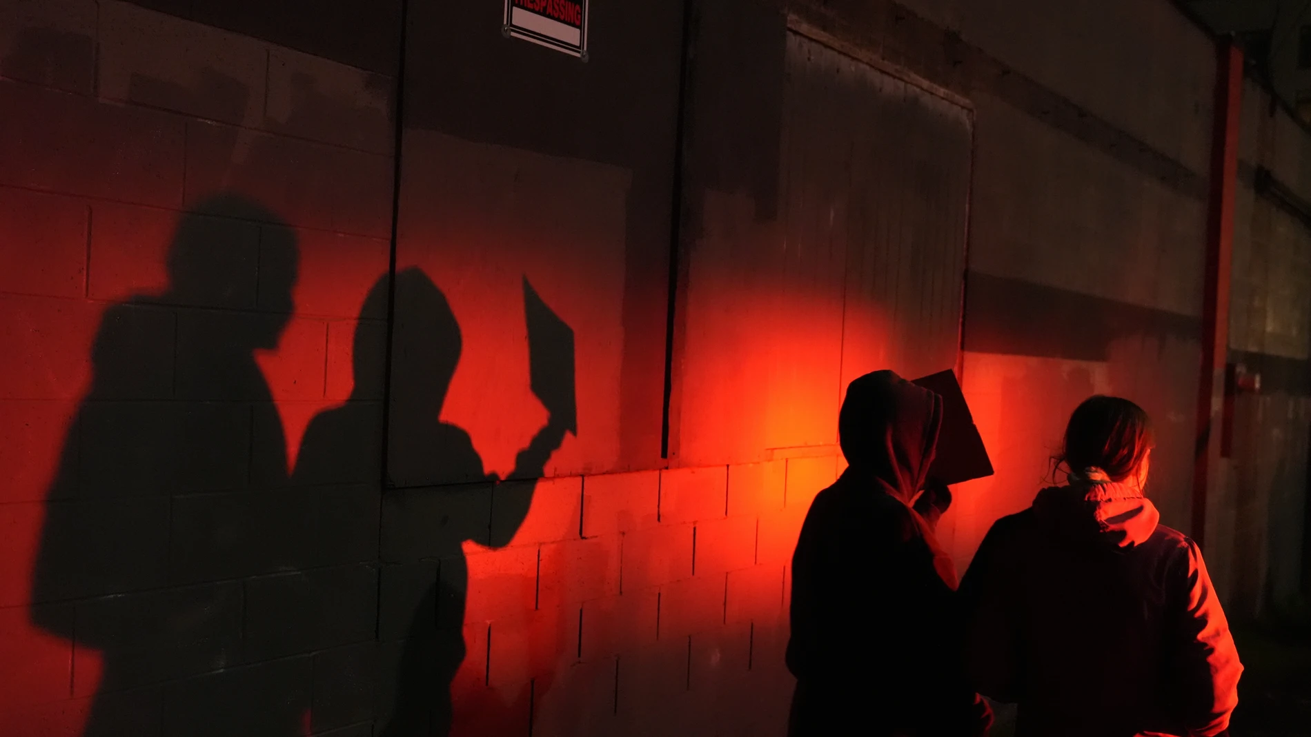 Two protesters are lit by a police light as they walk outside the U.S. Immigration and Customs Enforcement facility on Thursday, Jan. 8, 2026, in Portland, Ore. (AP Photo/Jenny Kane)