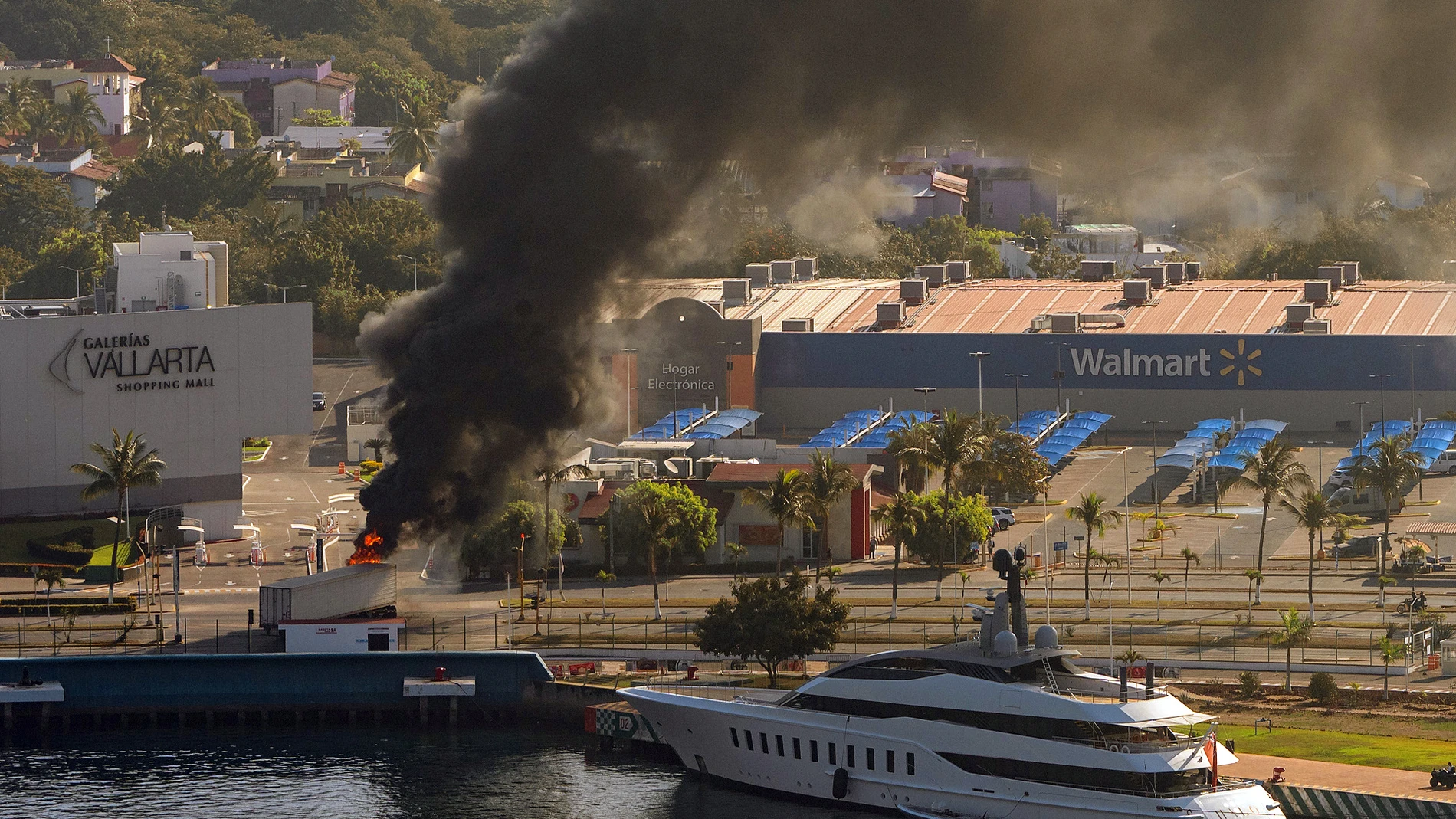 MEX5107. PUERTO VALLARTA (MÉXICO), 22/02/2026.- Fotografía aérea donde se ve camión incendiándose tras reacciones violentas por el abatimiento de Nemesio Rubén Oseguera Cervantes, alias 'El Mencho', líder del Cártel Jalisco Nueva Generación (CJNG) este domingo, en Puerto Vallarta (México). El abatimiento de alias El Mencho desató una ola de violencia y bloqueos carreteros en México. EFE/ Gerardo Santillán