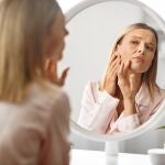 Mujer adulta observando un brote de acn&eacute; en el espejo del ba&ntilde;o