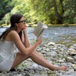 Mujer leyendo en la ribera del r&iacute;o
