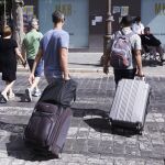 Dos turistas, con maletas, cruzan un paso de peatones