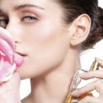 Mujer sosteniendo una rosa junto a un frasco de perfume