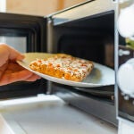 Una mujer mete un trozo de pizza en el microondas