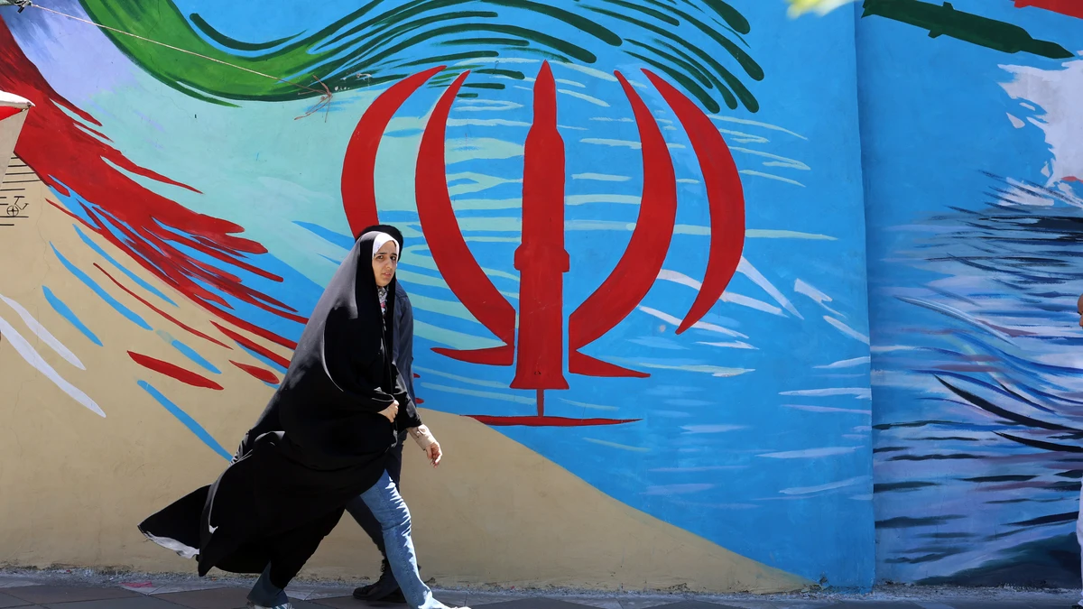 Una mujer iraní con velo camina junto a un mural de la bandera nacional de Irán en una calle de Teherán