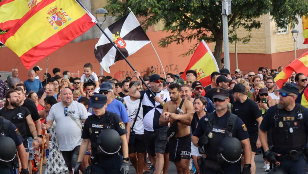 CEUTA, 25/08/2026.- Ceutíes protestan frente al acceso campamento temporal habilitado en la explanada de ‘Loma Colmenar’ con el lema “No invasión, expulsión.” Varios cientos de vecinos de Ceuta han trasladado este martes hasta la plaza de los Reyes, frente a la Delegación del Gobierno, la protesta c