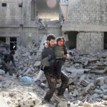 Un hombre lleva en brazos a un chico sobre los escombros de un edificio en Guta (Siria)