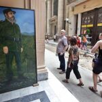 Turistas caminan por un boulevard, junto a una pintura de Fidel Castro en La Habana Vieja