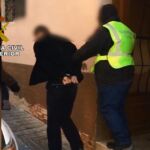 Un agente custodia al detenido tras el registro de su vivienda