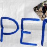 Un niño refugiado camina detrás de una pancarta en Idomeni