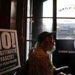 Un hombre en el interior de una cafetería en Los Ángeles con un cartel en contra de las políticas de Trump, el pasado día 17 de febrero