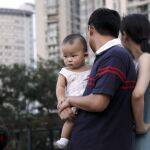 Una pareja observa a unos niños jugando en un parque cargando a su bebé en Shangai (China)
