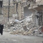 Varios civiles pasan por una calle con edificios en ruinas por los bombardeos en la zona de Maaret al-Numan, controlada por los rebeldes
