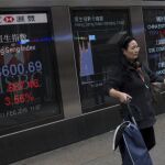 Una mujer camina junto a unas pantallas informativas que muestran la información bursátil en Hong Kong (China) el 11 de febrero de 2016