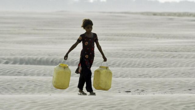 Una niña acarrea dos bidones para recoger agua en una seca región de India