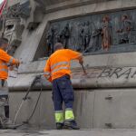 Operarios del servicio de limpieza del Ayuntamiento de Barcelona limpian las pintadas que han aparecido en el monumento a Cristóbal Colón