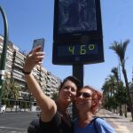 Dos jóvenes se hacen un selfi con el panel del termómetro de la calle que registra 46 grados en una zona del centro de Córdoba