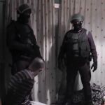 Dos agentes participantes en el operativo custodian a uno de los detenidos