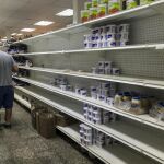 Los clientes buscan alimentos en un supermercado con las estanterías parcialmente vacías en Caracas (Venezuela).