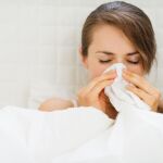Mujer en la cama sonándose la nariz