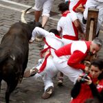 Un toro de la ganadería extremeña de Jandilla cornea a un mozo en el tramo de la Plaza Consistorial de Pamplona durante el séptimo encierro de los Sanfermines / Foto: Efe