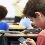 Un niño jugando con su teléfono móvil en clase / Dreamstime