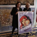 La alcaldesa de Madrid, Manuela Carmena (i), y de Barcelona, Ada Colau, posan junto al cartel regalo de Colau a la alcaldesa madrileña