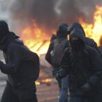 Manifestantes se cubren el rostro junto a un vehículo policial que arde ante la nueva sede del Banco Central Europeo (BCE) en Fráncfort (Alemania).