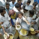 Familias damnificadas por las inundaciones reciben un plato de comida en un campo de refugiados paquistaní