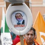 Un manifestante levanta una taza de váter con la imagen de Berlusconi en la que se puede leer «Caducado», en las protestas de ayer en Roma