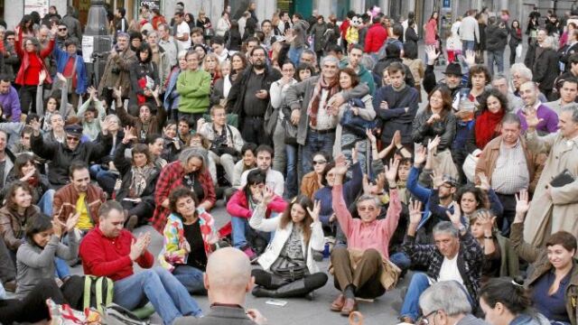Los «indignados» contaron ayer en su asamblea-mitin con el ex fiscal Anticorrupción Carlos Jiménez (sentado y con micro en mano). Abajo, uno de los carteles que el 15-M pegará desde el viernes y en el que critican a los banqueros, en la imagen la pancart