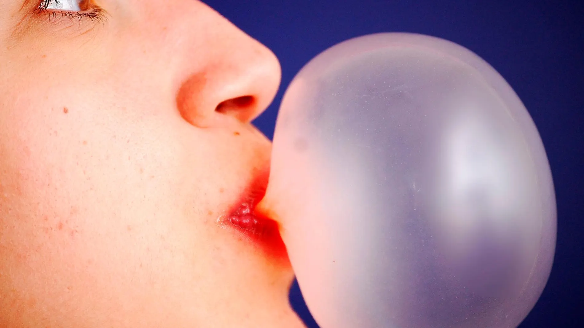 Una mujer haciendo una pompa con un chicle