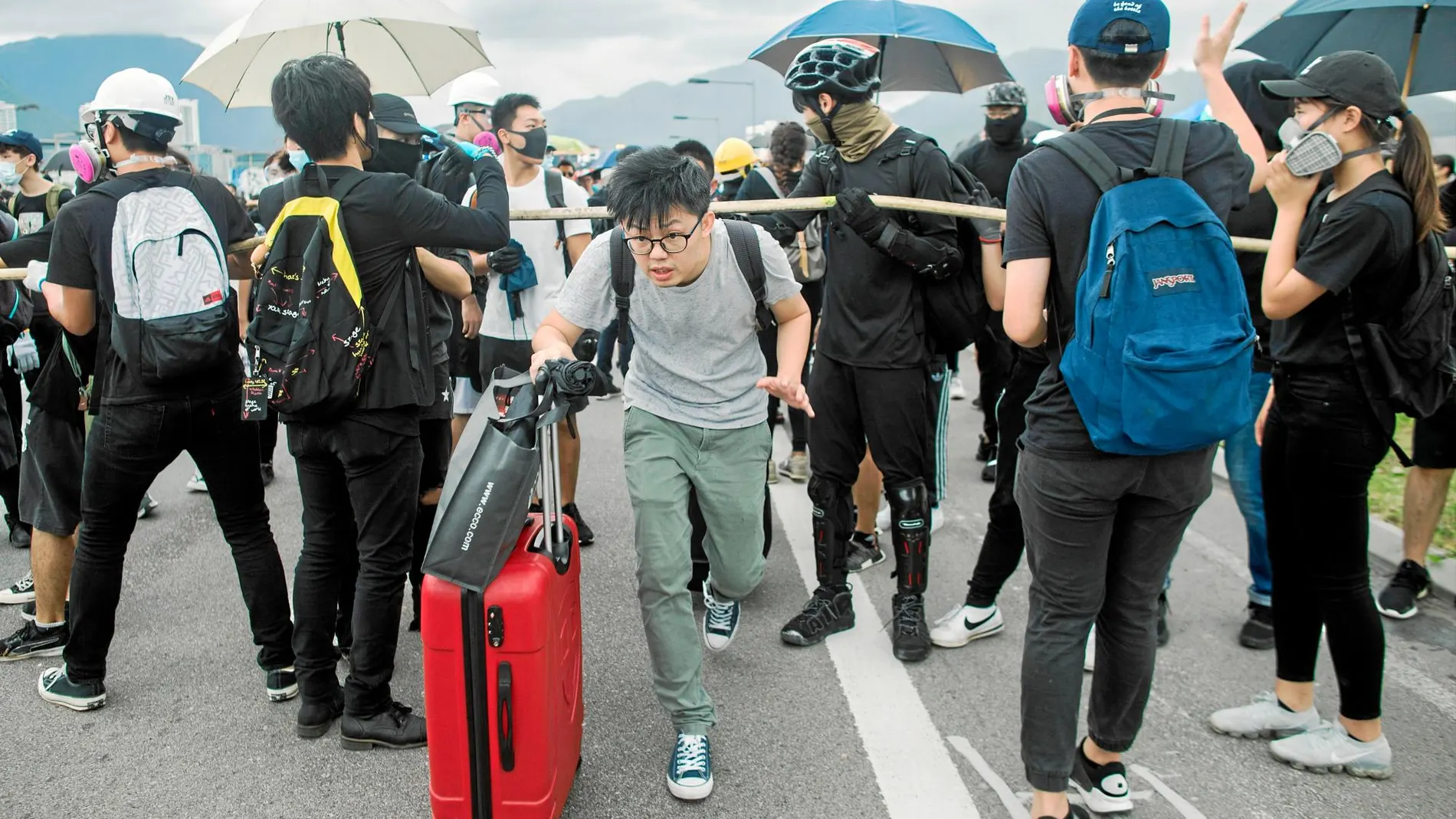 Un viajero trata ayer de esquivar a los manifestantes para acceder a la terminal de salidas del aeropuerto internacional de Hong Kong