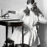 Una niña manipula una pequeña tabla apoyada y equipada con un lápiz vertical que se utilizaba tanto para la escritura automática como en sesiones de espiritismo