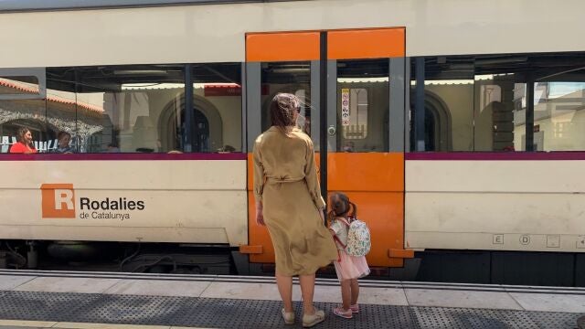 Una mujer y su hija en el anden de una estación junto a un tren de Rodalies