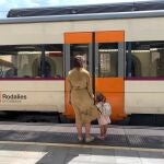 Una mujer y su hija en el anden de una estación junto a un tren de Rodalies