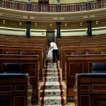 Vista del hemiciclo del Congreso de los Diputados vacío mientras una trabajadora lo limpia