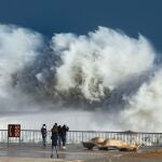 Varias personas observan las grandes olas en la playa de la Barceloneta, en Barcelona, este lunes, durante el fuerte temporal de Levante que azota Cataluña y que deja registros históricos de oleaje, viento y nieve.