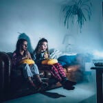 Jóvenes viendo la televisión en el sofá de su casa mientras beben zumo