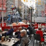 Varias personas disfrutan de un café en una terraza ante una de las numerosas fallas del barrio de Ruzafa, a la espera de los días grandes a partir de este próximo fin de semana