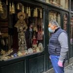 Un hombre con mascarilla contempla el escaparate de una tienda cofrade