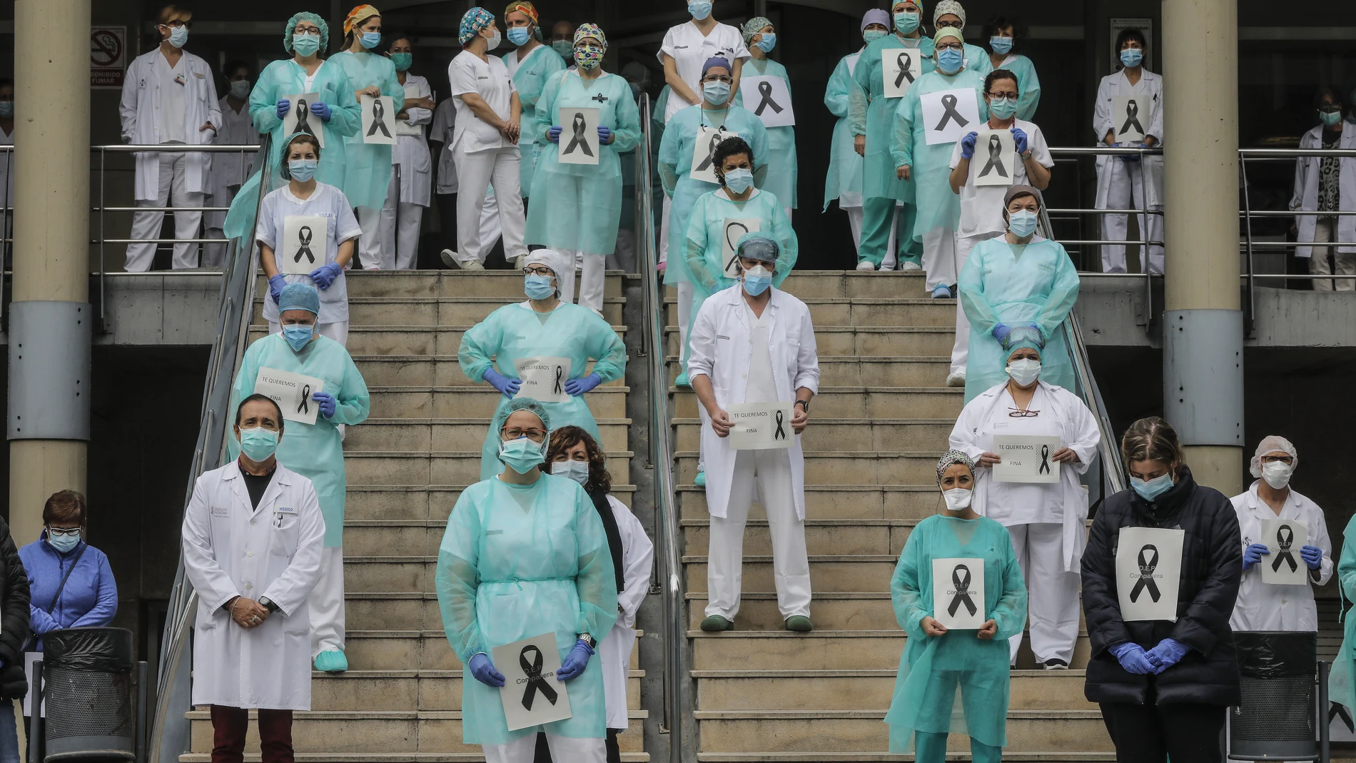 Sanitarios protegidos con mascarillas sujetan crespones negros durante el minuto de silencio en la entrada del Hospital Doctor Peset por la técnica de enfermería fallecida por coronavirus