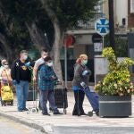 Varias personas esperan en una cola para entrar a un supermercado protegiéndose con mascarillas y guantes.