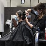 Una peluquera corta el pelo a una mujer con una máscara facial protectora contra el coronavirus.