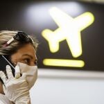 Una mujer con mascarilla y guantes habla por teléfono antes de coger un avión