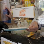 Una persona coge una mascarilla que le da una trabajadora de una farmacia