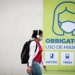 Una joven camina frente a un letrero que indica que el uso de la máscara es obligatorio en el transporte público este miércoles, en Sao Paulo